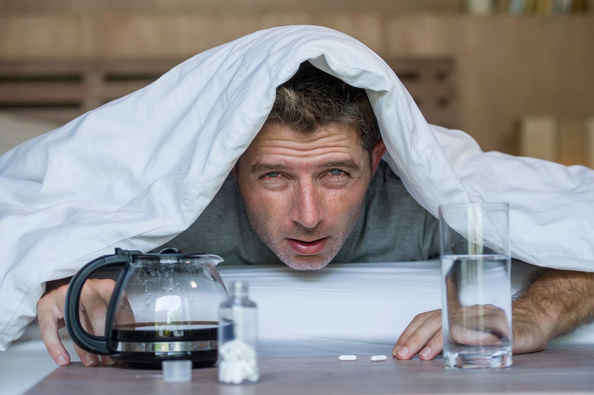lifestyle home portrait of young exhausted and wasted man waking up suffering headache and hangover after drinking alcohol at night party lying on bed sick and miserable still drunk